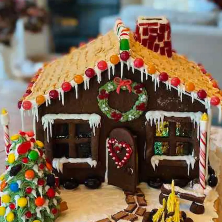 A festive, fully decorated gingerbread house complete with trees, path, fire, and lampposts.