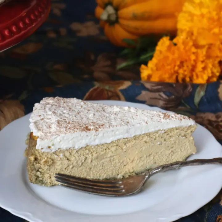 A close-up of a creamy slice of cheesecake topped with whipped cream and sprinkled with cinnamon.